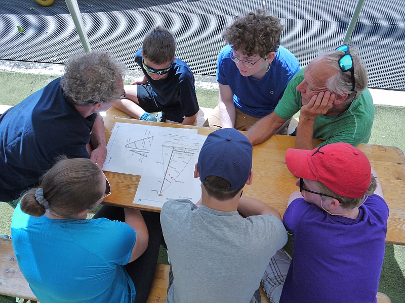 Teilnehmer und Segellehrer schauen sich Skizzen von Segelbooten an.